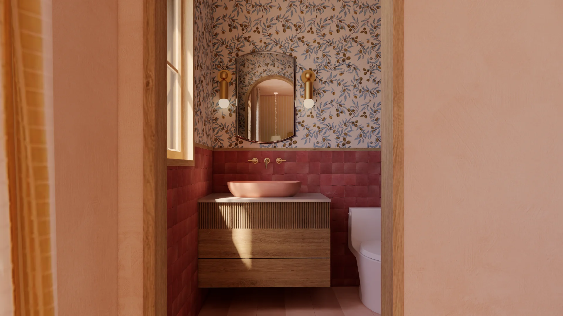 A modern bathroom features warm terracotta and burgundy tones, with a floating wooden vanity topped by a round ceramic sink and arched mirror with gold hardware, set against walls of botanical-patterned wallpaper in the upper half and deep red tile in the lower half.