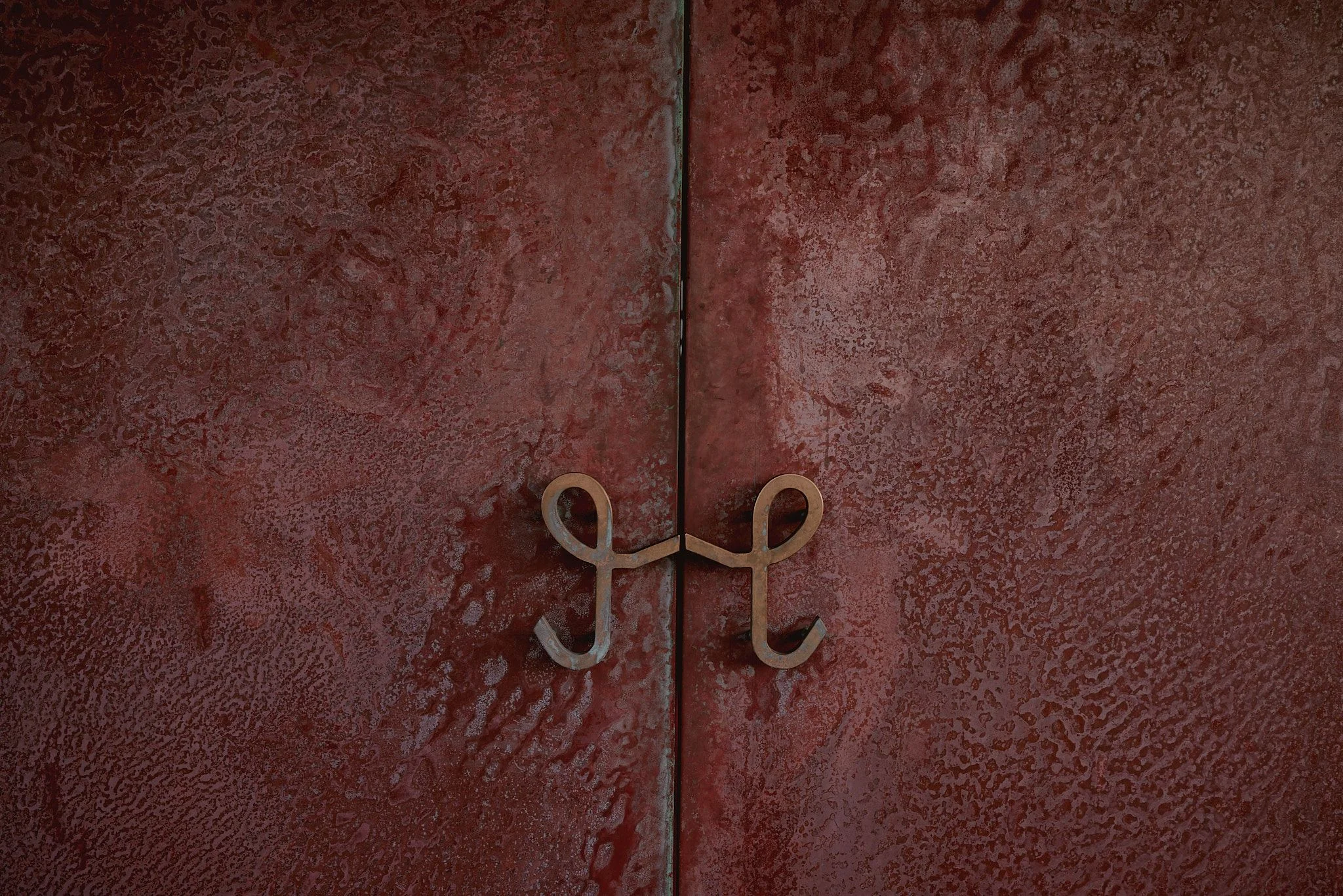 A pair of ornate brass loop handles centered on two deep burgundy cabinet doors with a textured, weathered finish and a vertical seam dividing them.